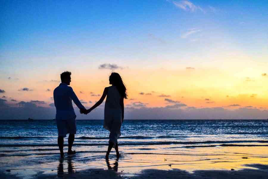 Man and woman holding hands and walking on a beach.