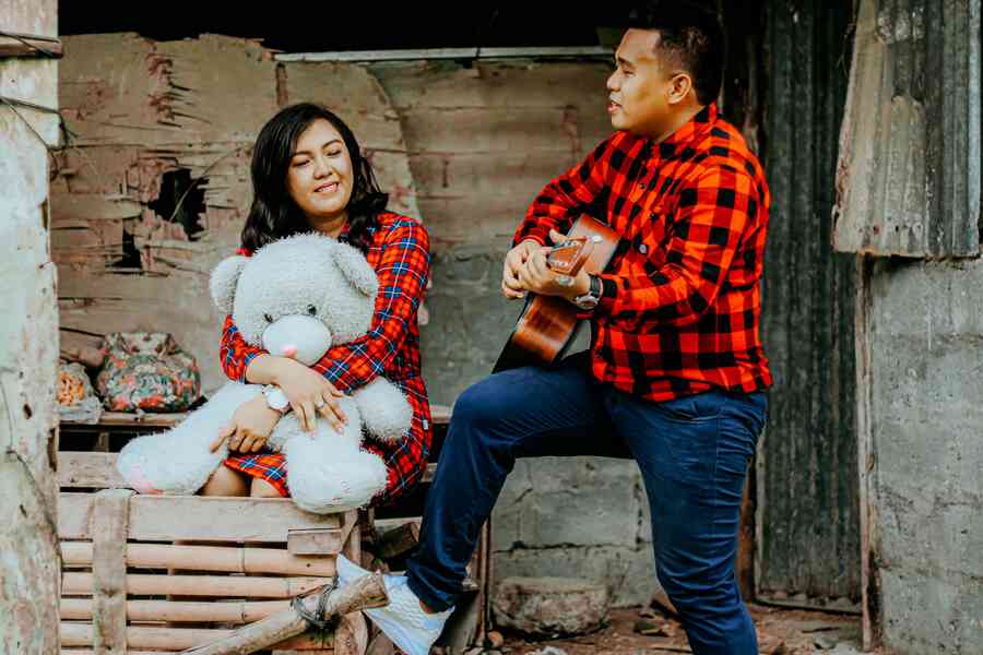 Romantic couple with man playing a guitar to a woman holding a stuffed bear